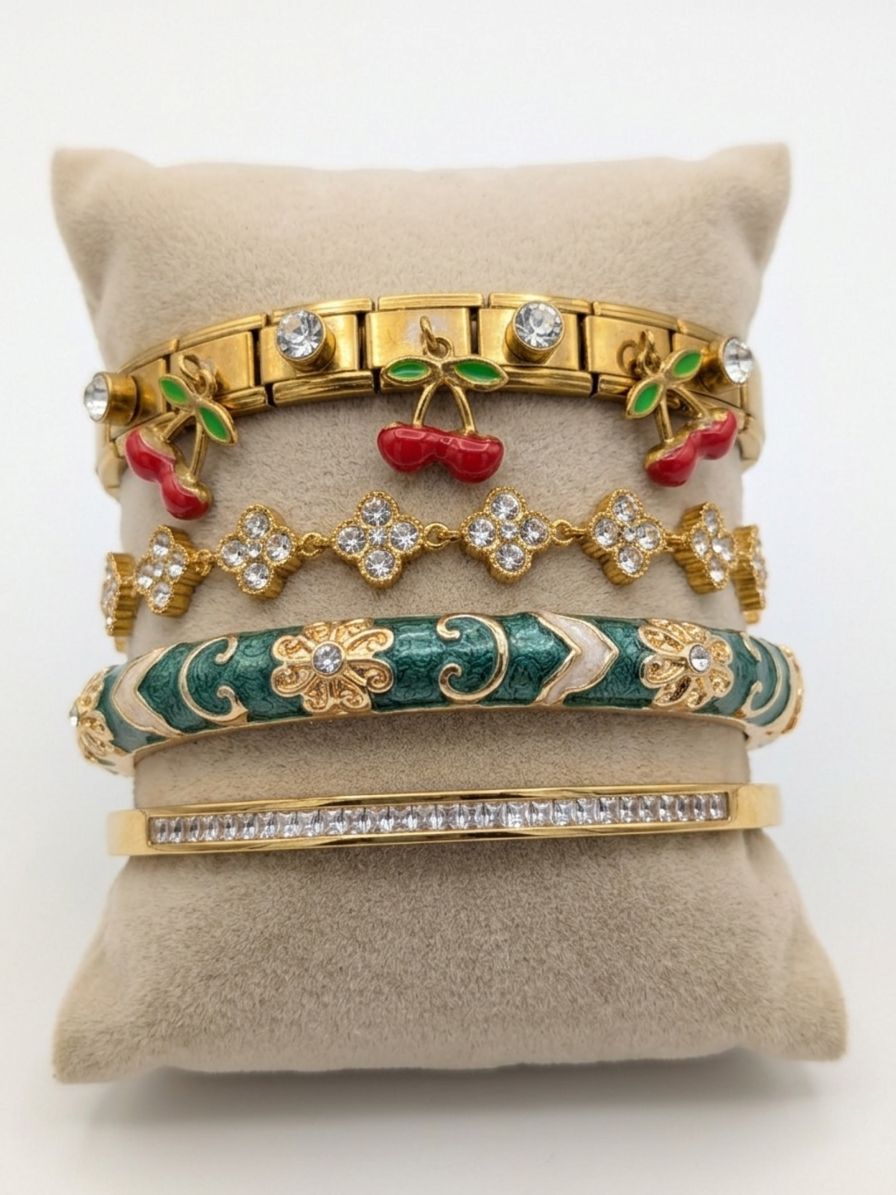 Composition de bracelets dorés élégants pour femme, incluant un bracelet orné de breloques cerises rouges émaillées et de cristaux, présenté sur un coussin en lin.